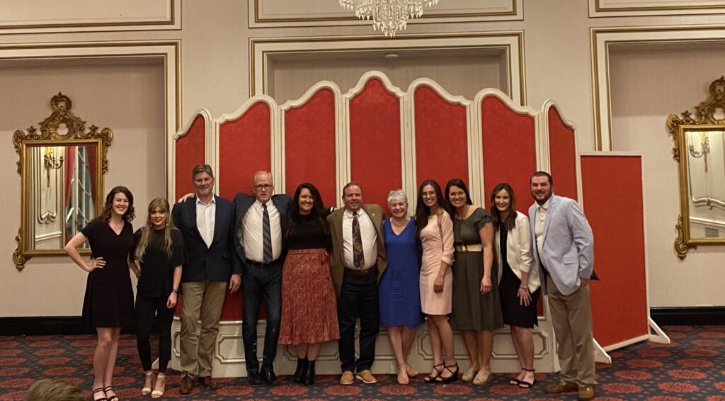 Group photo of GAE Architecture + Design team members posing in a formal setting with red and gold decor, showcasing company culture and teamwork.