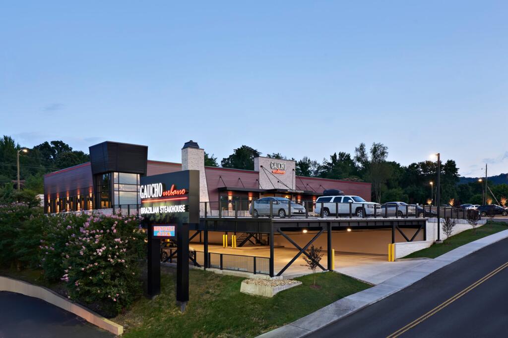 Gaucho Urbano Brazilian Steakhouse exterior view with modern architecture, featuring a prominent sign and elevated parking area, designed and built by George Ewart, a top commercial architect firm in Knoxville, TN.