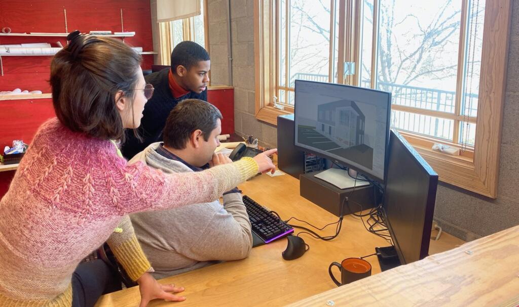 Group of architecture students collaborating at a computer, reviewing a 3D model of a building design, showcasing teamwork and innovation in architecture and design.