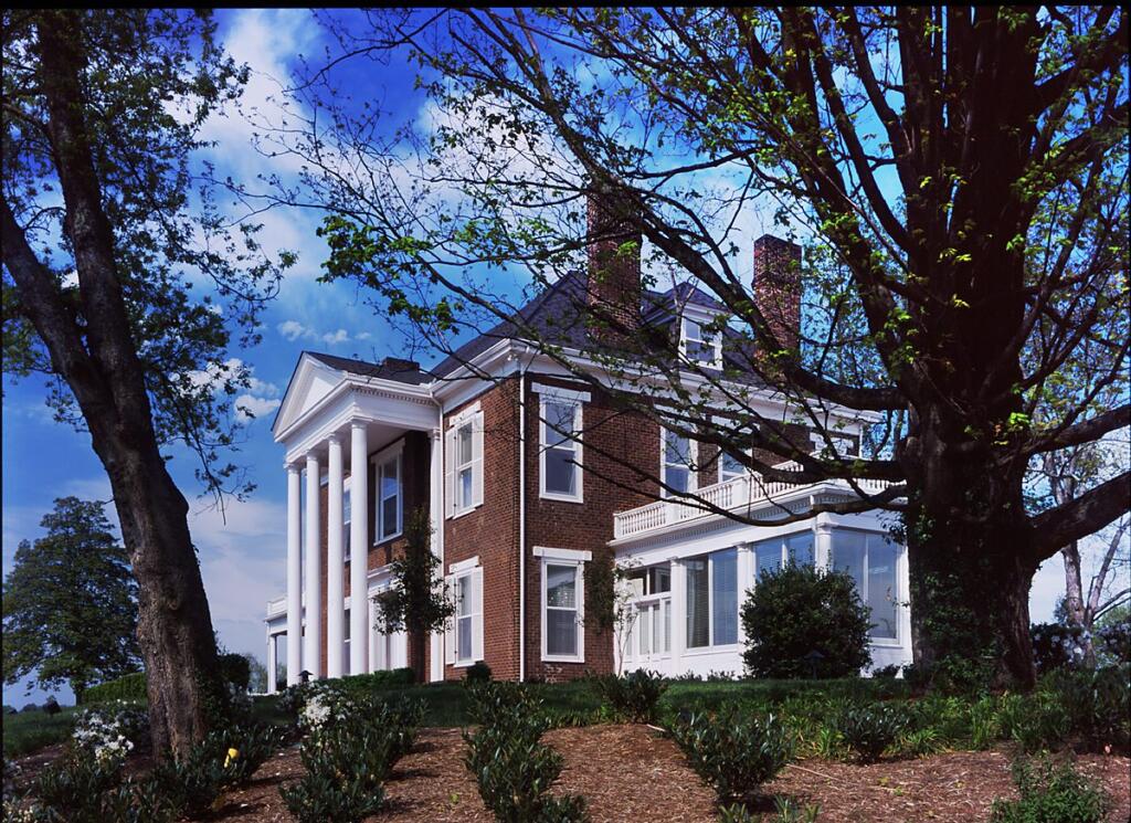 Historic brick house with white columns and balcony, surrounded by trees and landscaping, showcasing architectural design by GAE Architecture + Design, a top commercial architect firm in Knoxville, TN.