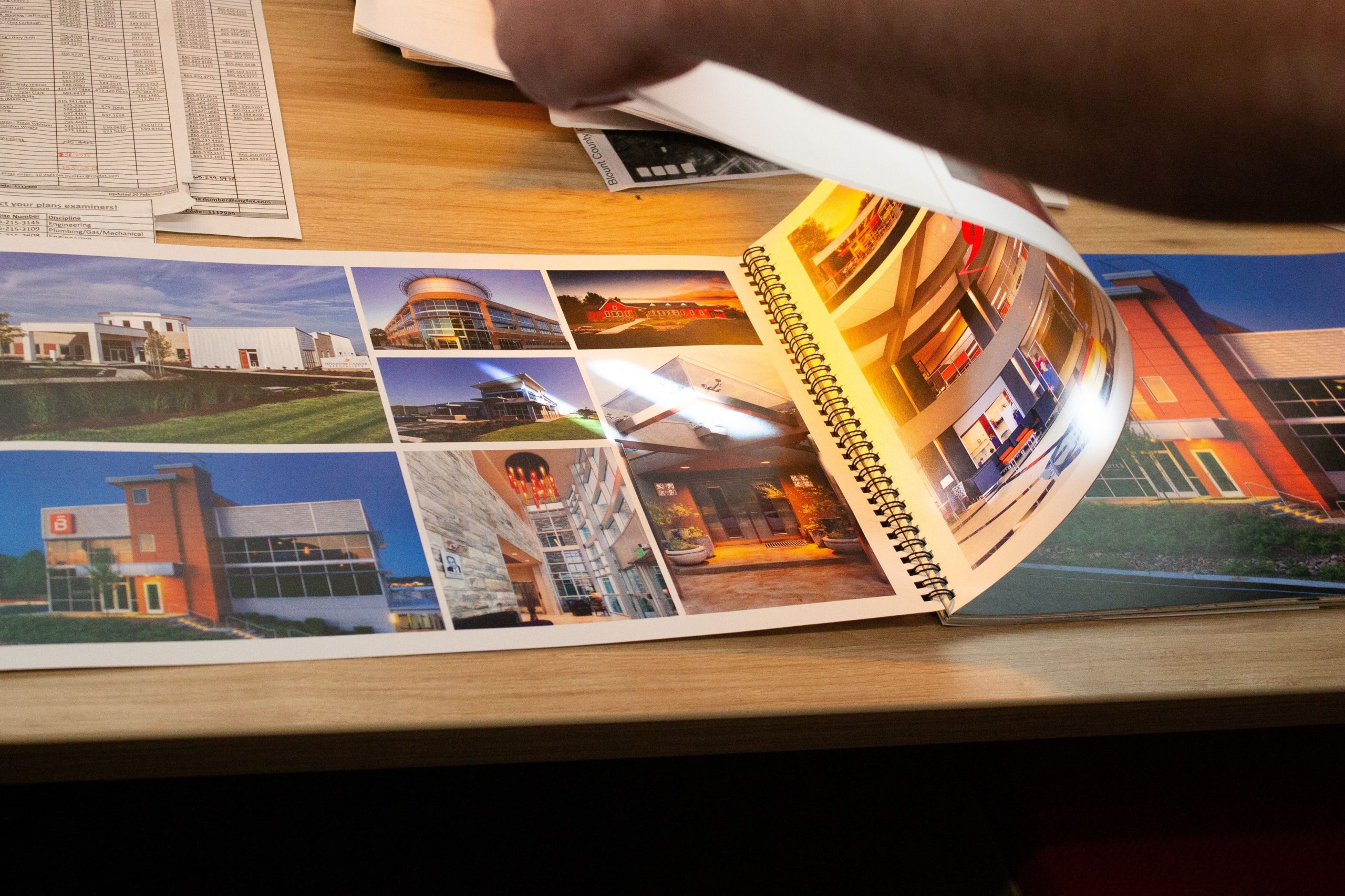 Hand flipping through an architectural design portfolio showcasing various awe-inspiring buildings and urban spaces, emphasizing GAE Architecture + Design's focus on impactful architecture.