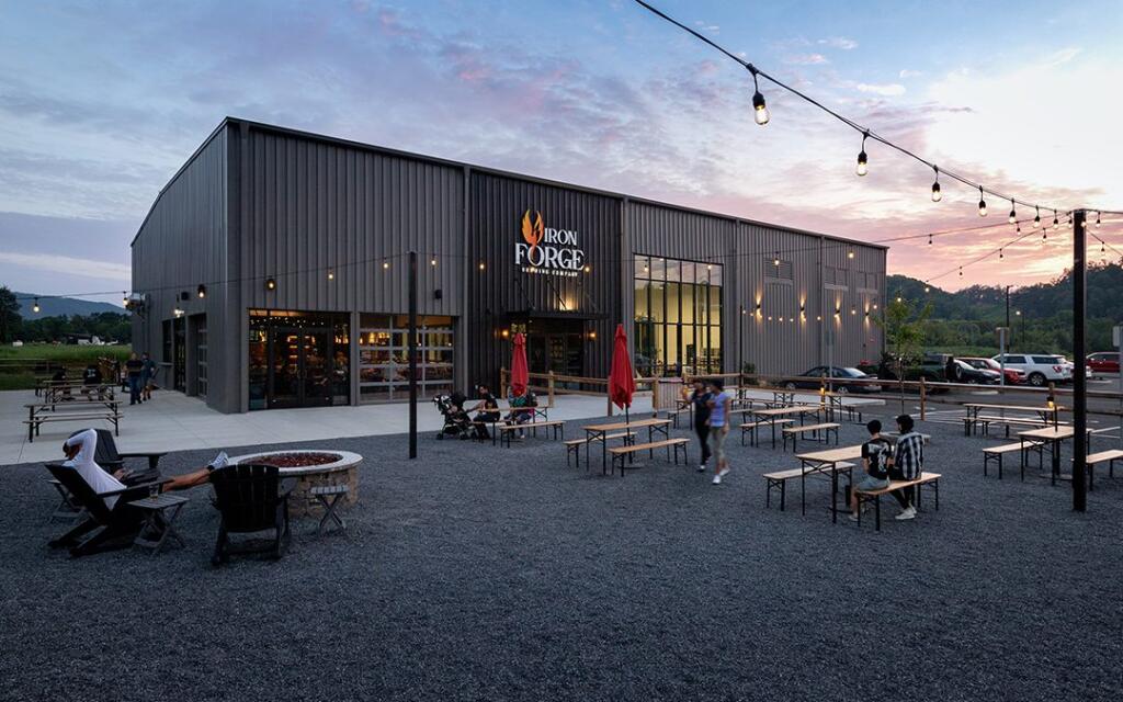 Exterior view of Iron Forge restaurant featuring modern architecture, outdoor seating with tables and chairs, patrons enjoying the space, and a sunset backdrop, designed and built by George Ewart, a top commercial architect firm in Knoxville, TN.