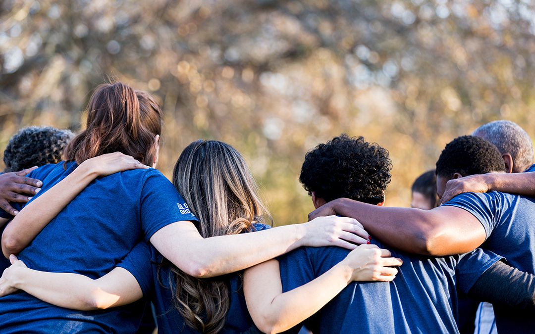 Group of diverse individuals in blue shirts embracing each other, showcasing teamwork and community spirit, reflecting GAE Architecture + Design's commitment to giving back and fostering a collaborative environment in Knoxville, TN.