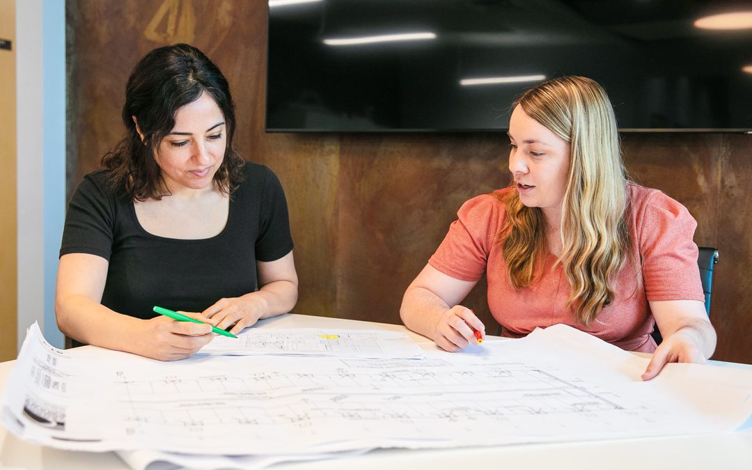 Two women collaborating over architectural blueprints, highlighting women's contributions in architecture and design at GAE Architecture + Design during Women's History Month.