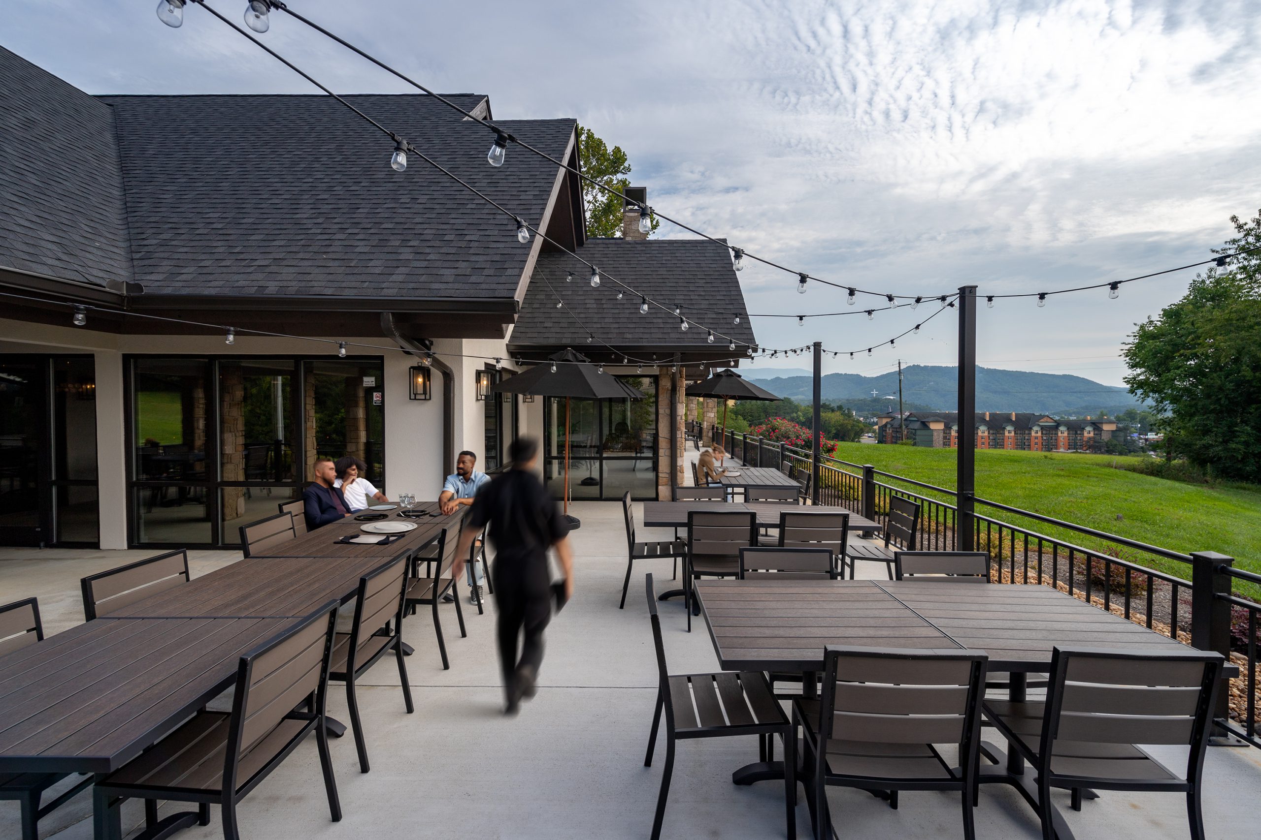 Outdoor dining area of Pizza Rio featuring modern tables and chairs, string lights overhead, with guests enjoying the view of the landscape in Pigeon Forge, designed and built by George Ewart, a top commercial architect firm in Knoxville, TN.