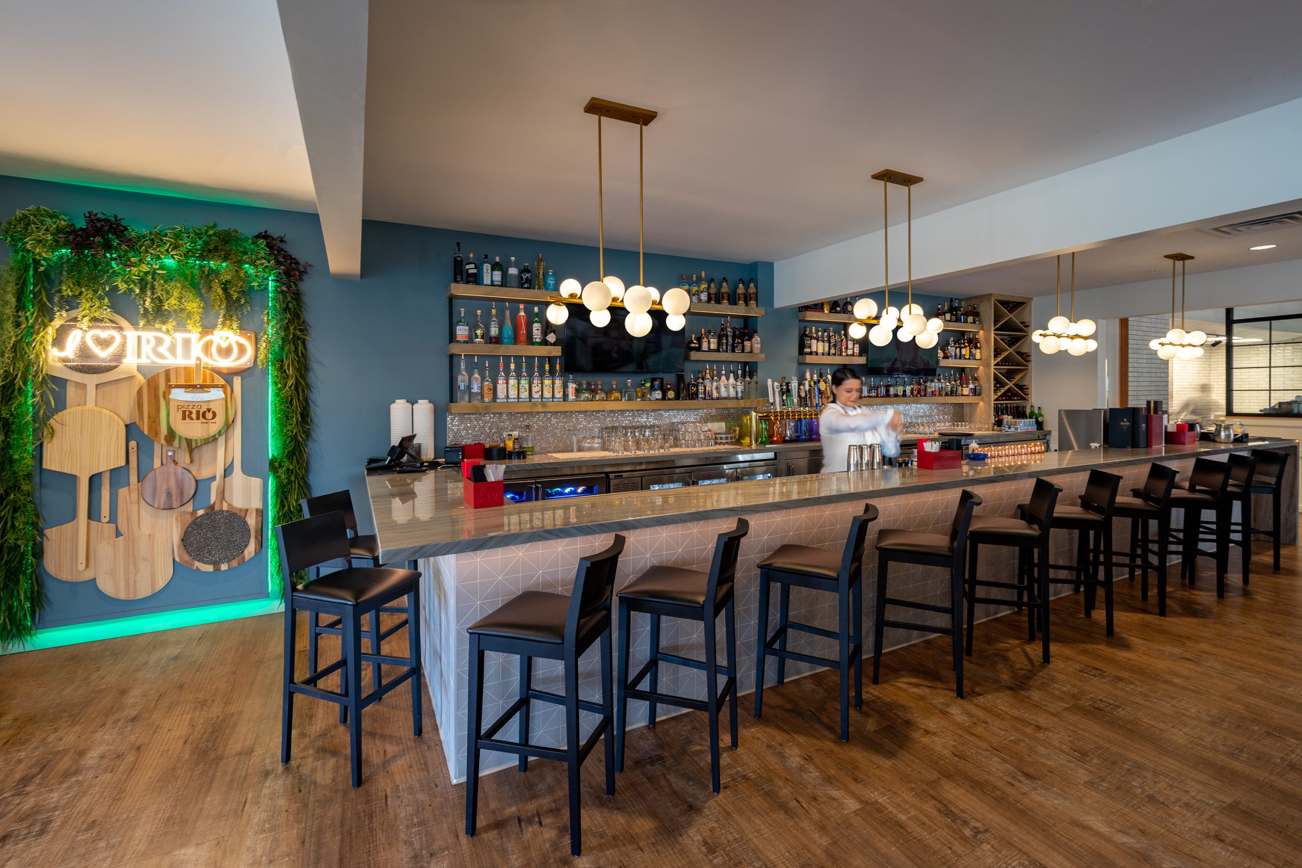 Bar area in Pizza Rio featuring a vibrant cocktail selection, illuminated signage, and a stylish countertop, designed and built by George Ewart, a top commercial architect firm in Knoxville, TN.