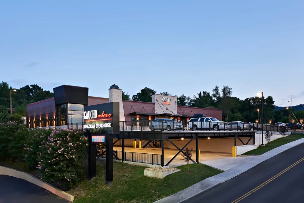 Gaucho Urbano Brazilian steakhouse exterior in Pigeon Forge, featuring a modern design, prominent glass walls, and a two-story parking garage integrated into the hillside, designed and built by George Ewart, a top commercial architect firm in Knoxville, TN.