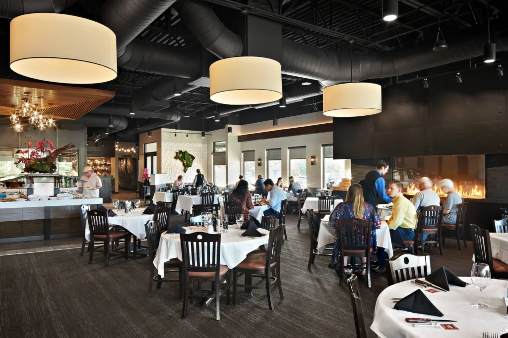 Interior view of Gaucho Urbano restaurant in Pigeon Forge, featuring elegantly set tables, modern lighting, and a visible kitchen area with a grilling station, designed and built by George Ewart, a top commercial architect firm in Knoxville, TN.