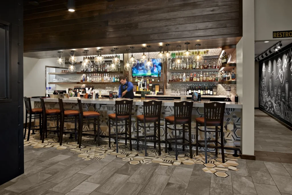 Bar area of Gaucho Urbano in Pigeon Forge, featuring a bartender preparing drinks, stylish hexagonal tile flooring, and a well-stocked back bar with various spirits, designed and built by George Ewart, a top commercial architect firm in Knoxville, TN.