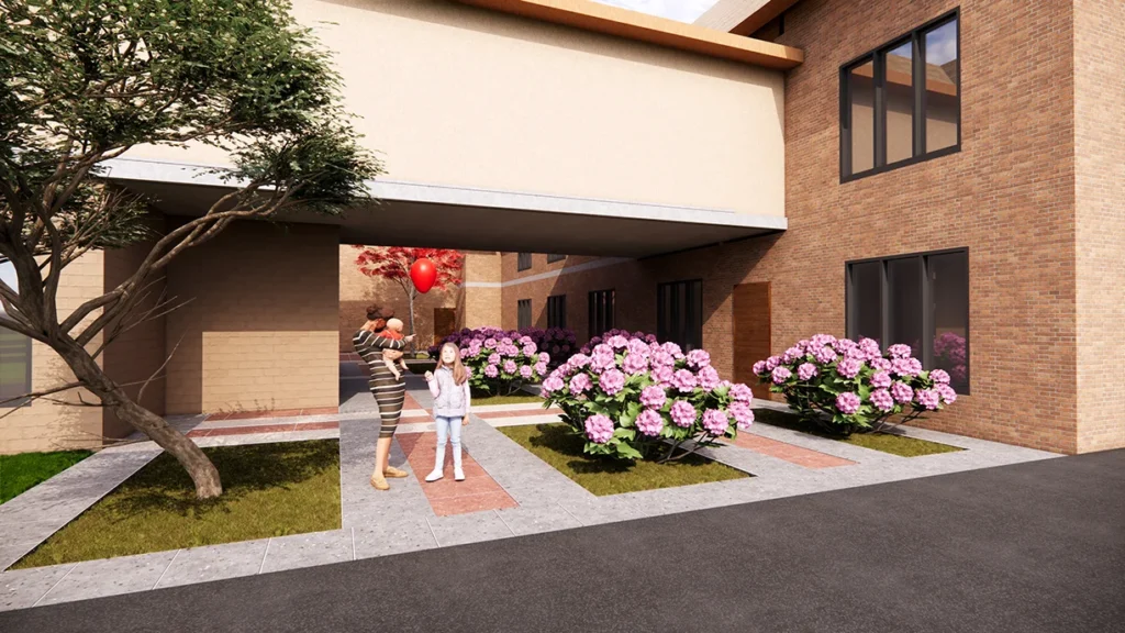 Family Life Center entrance at St. Joseph the Worker Catholic Church, featuring a woman holding a baby and a girl with a balloon, surrounded by flowering shrubs and modern architectural design, emphasizing community space and connectivity, designed and built by George Ewart, a top commercial architect firm in Knoxville, TN.