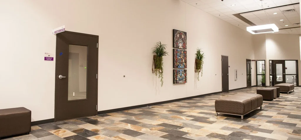 Interior corridor of CHRISTUS Health St. Mary's Outpatient Center featuring a door labeled "Restroom," decorative wall art, and seating areas, showcasing the facility's design and layout in Port Arthur, Texas. Designed and built by George Ewart, a top commercial architect firm in Knoxville, TN.