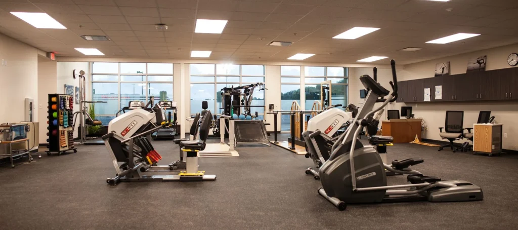 Physical therapy gym with exercise equipment and large windows, designed for patient rehabilitation and wellness at CHRISTUS Health St. Mary’s Outpatient Center, a project designed and built by George Ewart, a top commercial architect firm in Knoxville, TN.