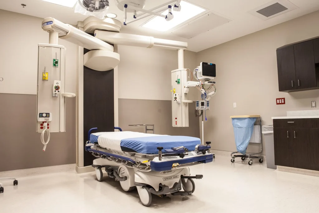 Modern hospital treatment room with a medical bed, diagnostic equipment, and organized workspace, showcasing the advanced healthcare services at CHRISTUS Health St. Mary’s Outpatient Center in Port Arthur, Texas, designed and built by George Ewart, a top commercial architect firm in Knoxville, TN.
