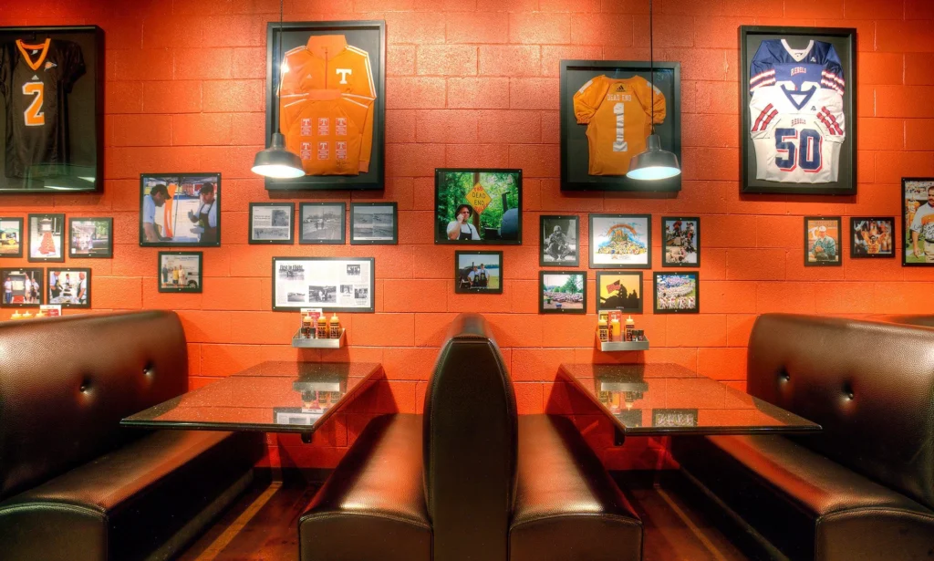 Interior of Dead End BBQ restaurant in Knoxville, TN, featuring orange walls adorned with framed sports jerseys and photographs, showcasing local history and community connections, designed and built by George Ewart, a top commercial architect firm in Knoxville, TN.