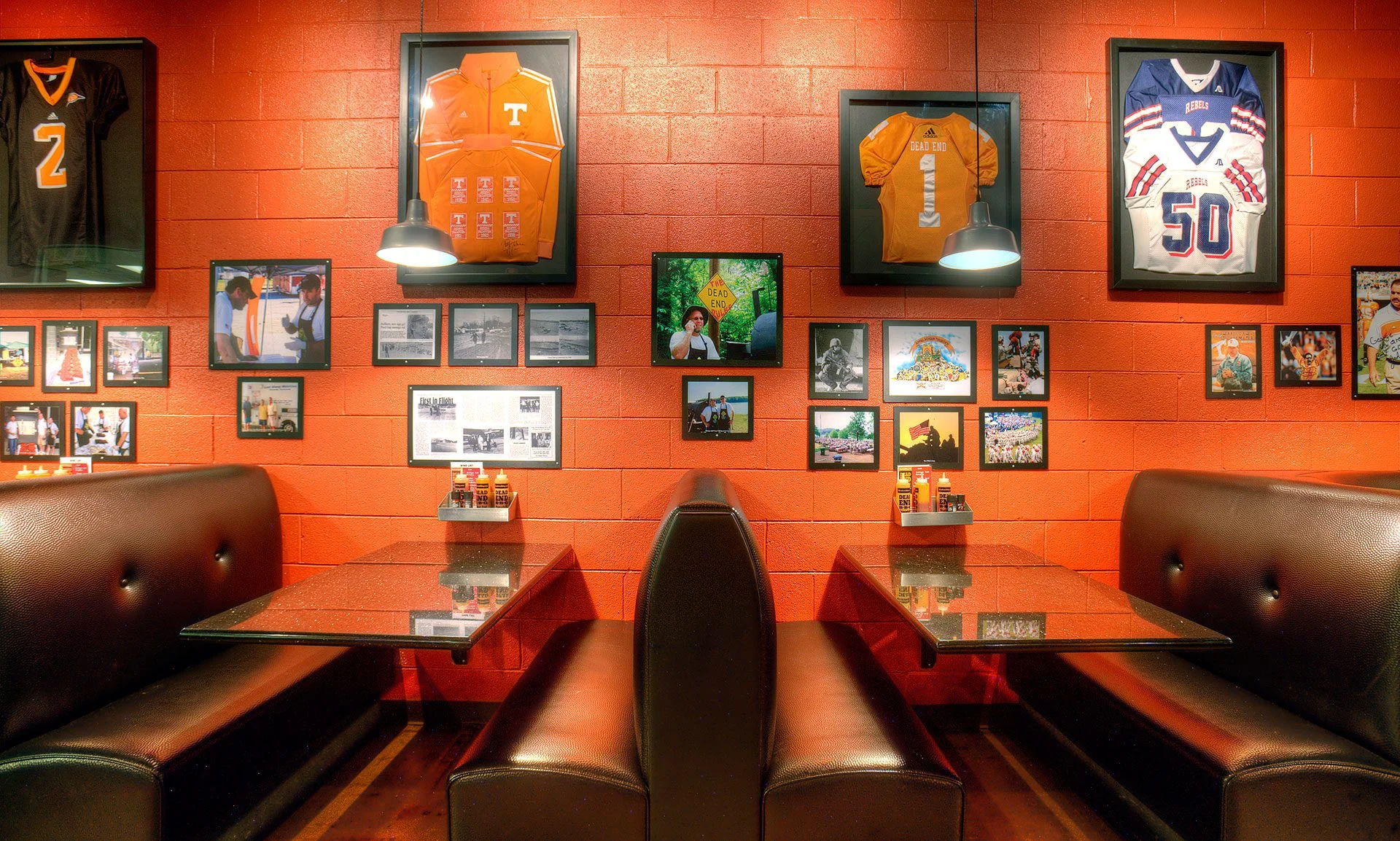 Interior view of Dead End BBQ restaurant in Knoxville, TN, featuring black booths, orange walls adorned with framed sports jerseys, historical photographs, and local memorabilia, emphasizing community connection and comfort in a welcoming dining atmosphere, designed and built by George Ewart, a top commercial architect firm in Knoxville, TN.