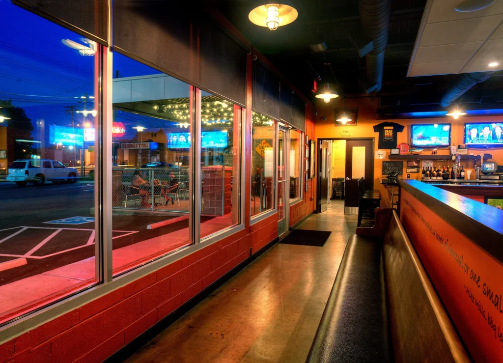 Interior view of Dead End BBQ restaurant in Knoxville, TN, showcasing a vibrant dining area with exposed brick walls, large windows, and a bar, designed to create a welcoming community atmosphere, emphasizing transparency and connection, designed and built by George Ewart, a top commercial architect firm in Knoxville, TN.