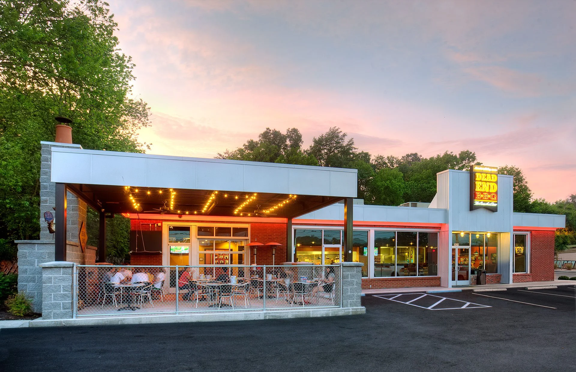 Exterior view of Dead End BBQ restaurant, featuring a modern design with outdoor seating, string lights, and a prominent sign, showcasing the architectural transformation by GAE Architecture + Design, emphasizing community connection in Knoxville, TN.