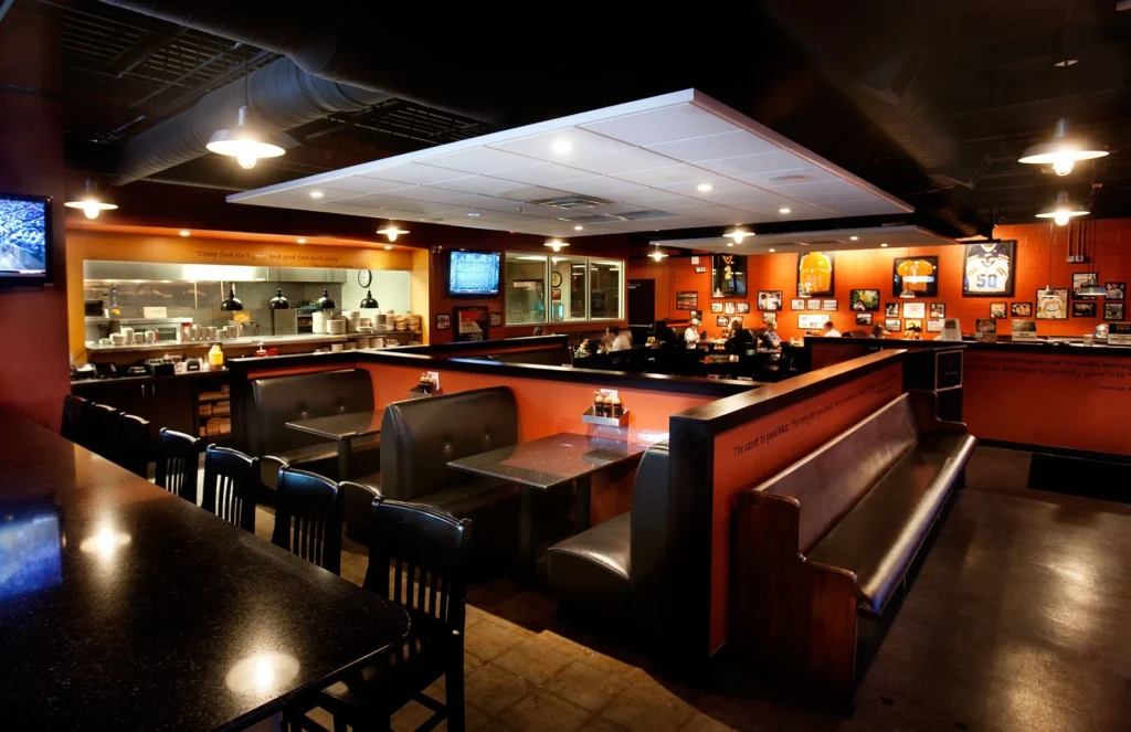 Interior view of Dead End BBQ restaurant in Knoxville, TN, featuring open dining area with booths, a visible smoke room for pitmasters, and walls adorned with local sports memorabilia, designed and built by George Ewart, a top commercial architect firm in Knoxville, TN.