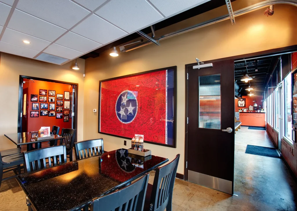 Interior of Dead End BBQ restaurant in Knoxville, TN, featuring a black granite table, wooden chairs, a Tennessee flag artwork on the wall, and a gallery of community photos, designed and built by George Ewart, a top commercial architect firm in Knoxville, TN.