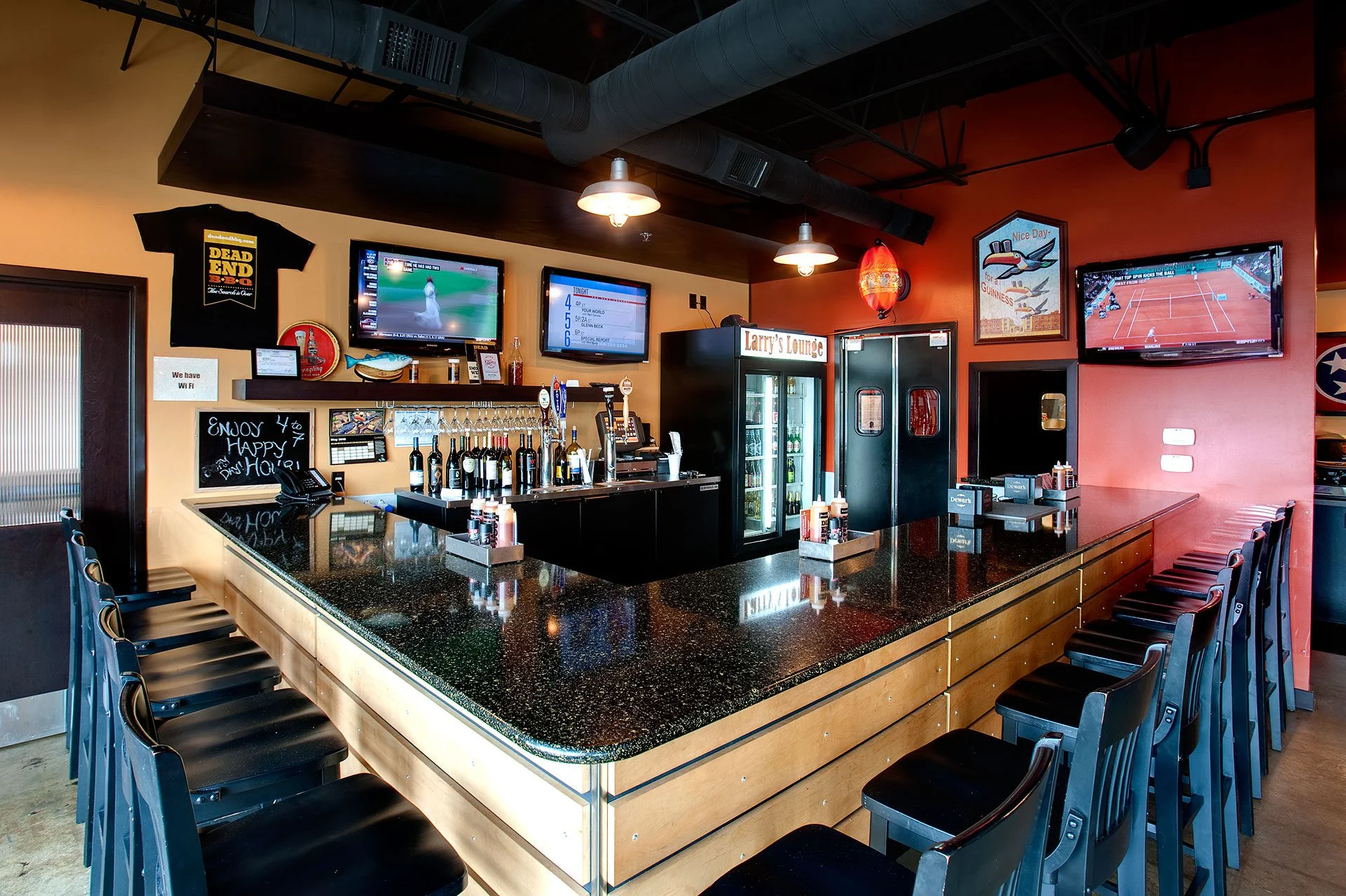 Bar area of Dead End BBQ featuring a granite countertop, bar stools, multiple televisions displaying sports, and a visible drink station, designed to create a welcoming atmosphere in Knoxville, TN.