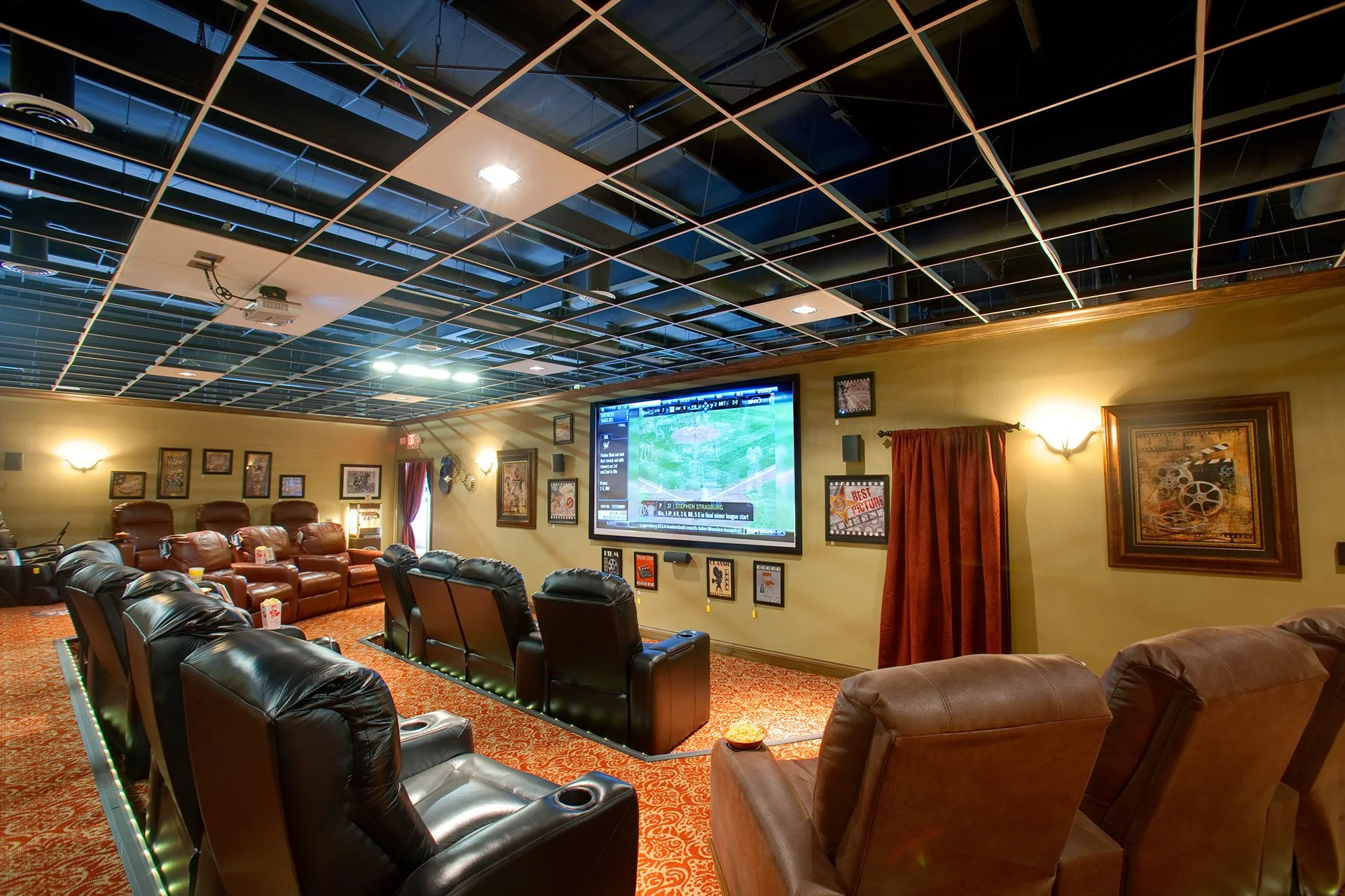 Home theater seating arrangement with a large screen displaying a sports event, surrounded by decorative wall art and ambient lighting, showcasing immersive entertainment design by GAE Architecture + Design, a top commercial architect firm in Knoxville, TN.