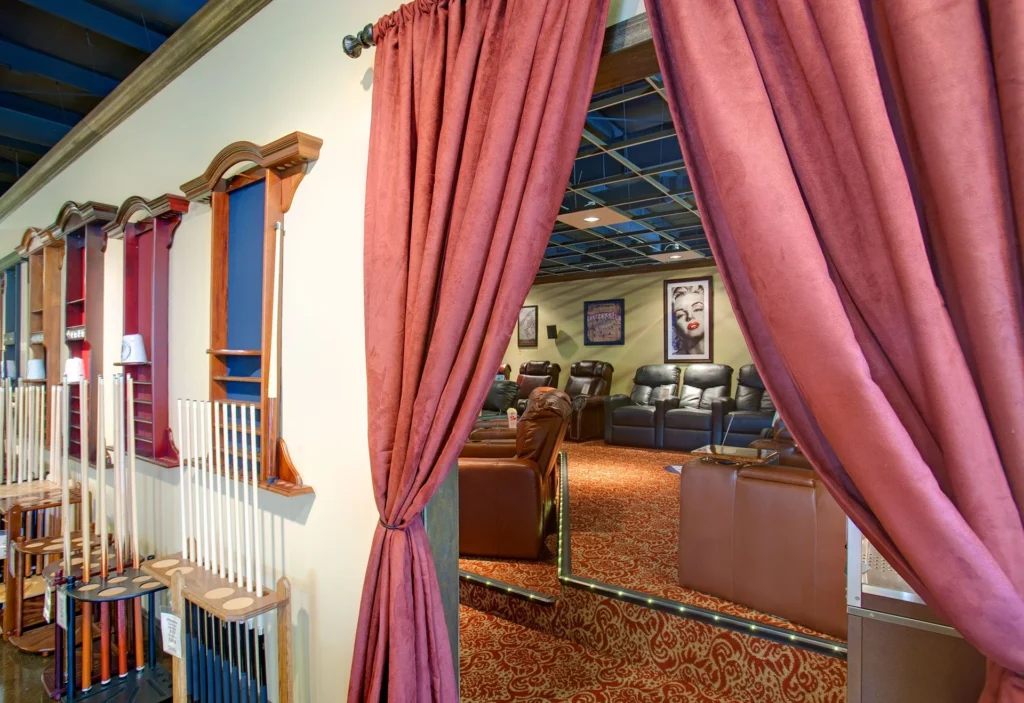 Interior view of a home movie theater showroom, featuring plush seating, decorative curtains, and pool table accessories, designed and built by George Ewart, a top commercial architect firm in Knoxville, TN.