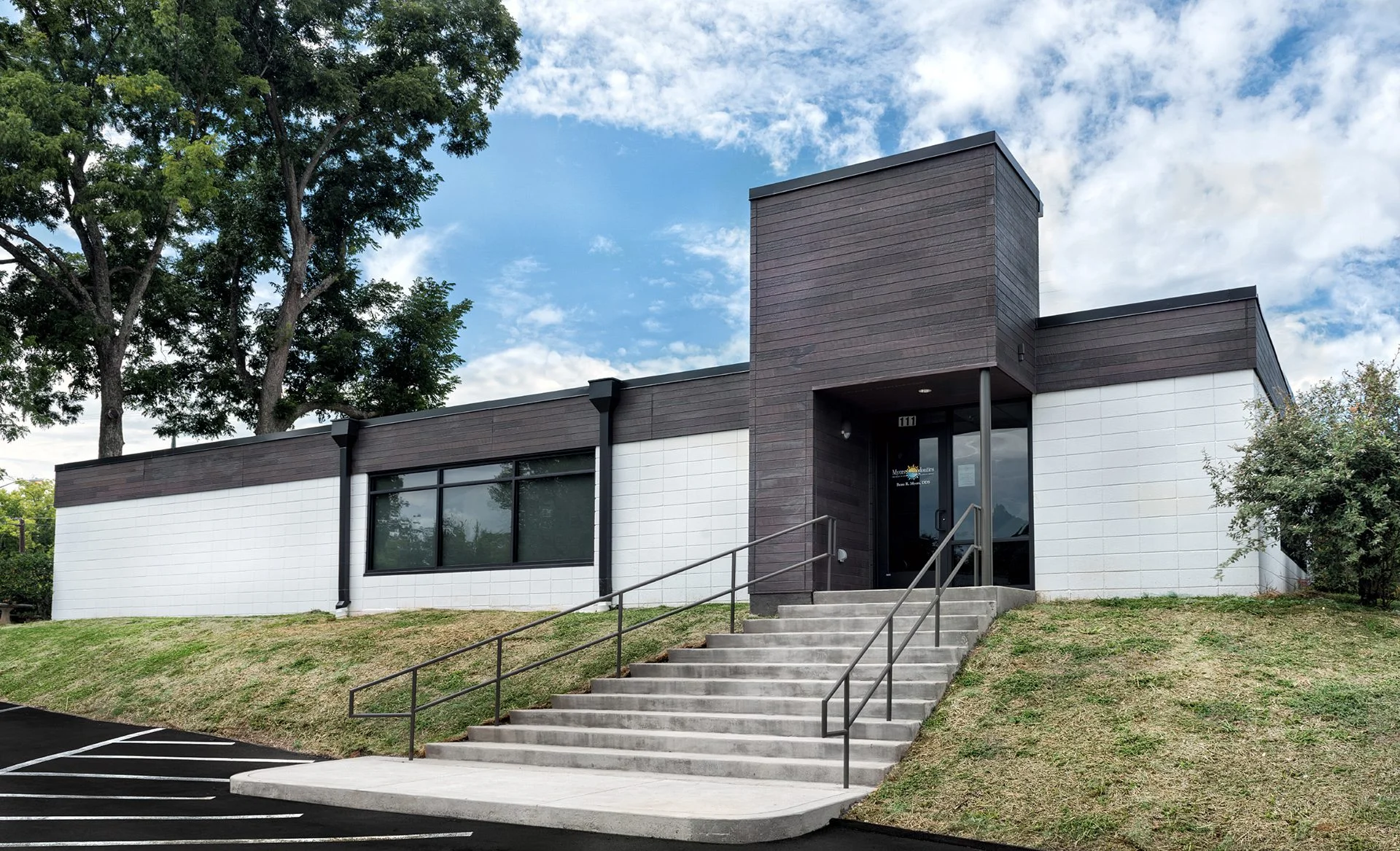 Modern exterior of Myers Orthodontics building, featuring a blend of dark wood and white walls, accessible ramp, and landscaped surroundings, designed and built by George Ewart, a top commercial architect firm in Knoxville, TN.