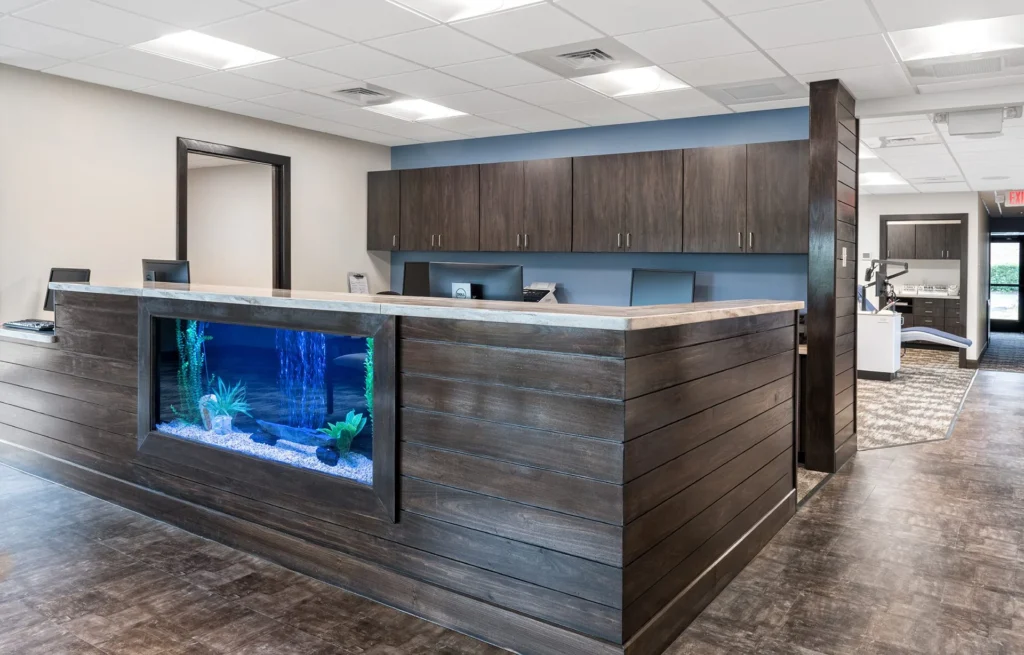 Reception area of Myers Orthodontics featuring a modern design with a wooden reception desk, aquarium, and cabinetry, emphasizing a welcoming atmosphere, designed and built by George Ewart, a top commercial architect firm in Knoxville, TN.