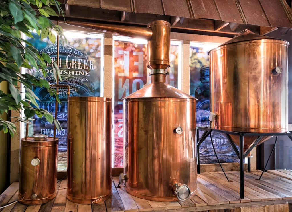 Copper distilling equipment at Smith Creek Moonshine, featuring multiple stills and an immersive rustic design, reflecting the Smoky Mountains' influence in the Pigeon Forge retail space, designed and built by George Ewart, a top commercial architect firm in Knoxville, TN.