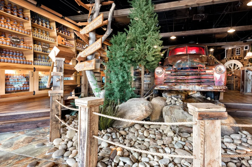 Rustic interior of Smith Creek Moonshine featuring a vintage pickup truck as a focal point, surrounded by stone landscaping and wooden signage, showcasing product displays inspired by the Smoky Mountains, designed and built by George Ewart, a top commercial architect firm in Knoxville, TN.