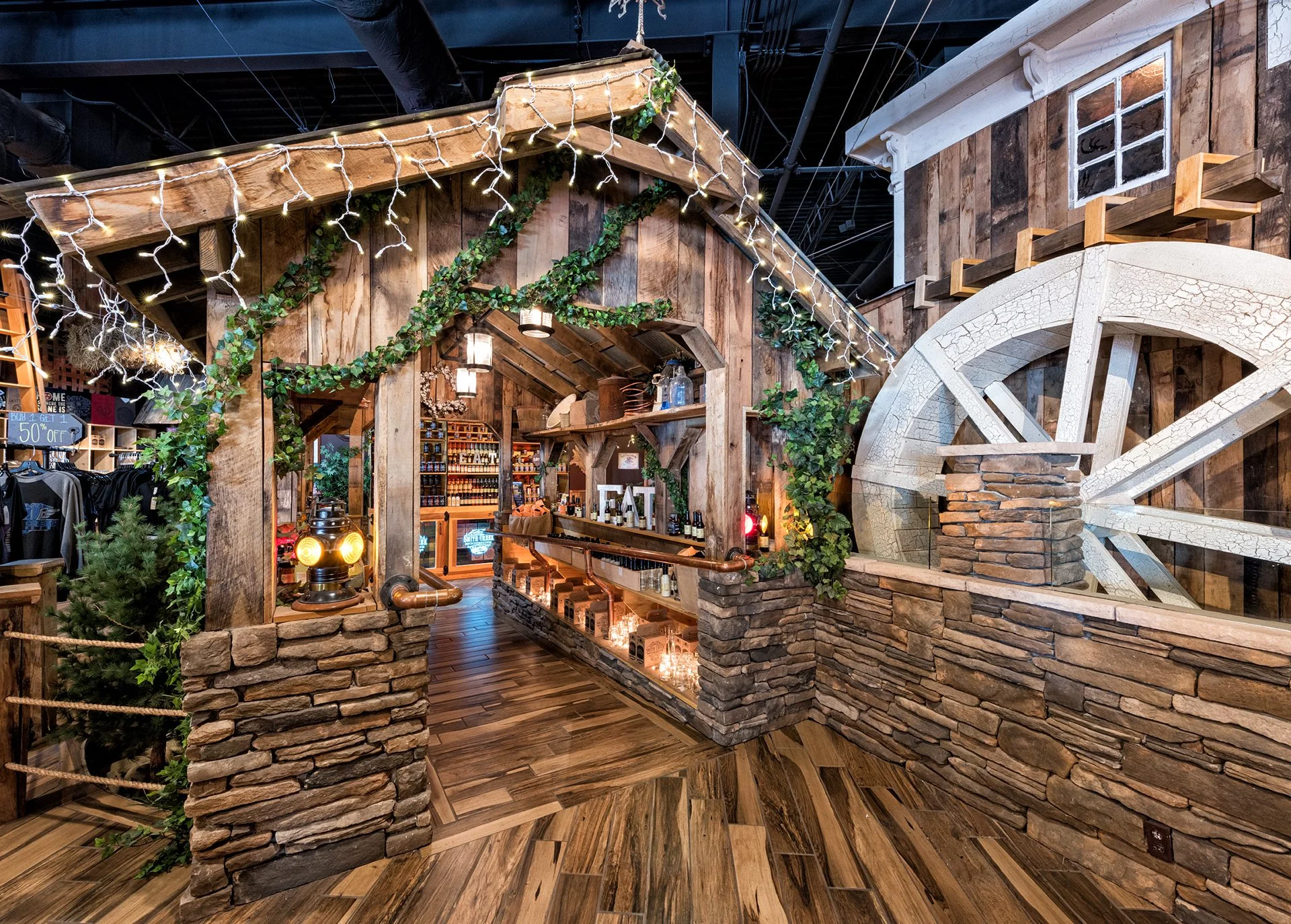 Rustic retail interior of Smith Creek Moonshine featuring a wooden structure, stone accents, and a communal tasting bar, designed to reflect the Smoky Mountains' inspiration, with decorative lights and greenery, showcasing the immersive experience by GAE Architecture + Design, a top commercial architect firm in Knoxville, TN.