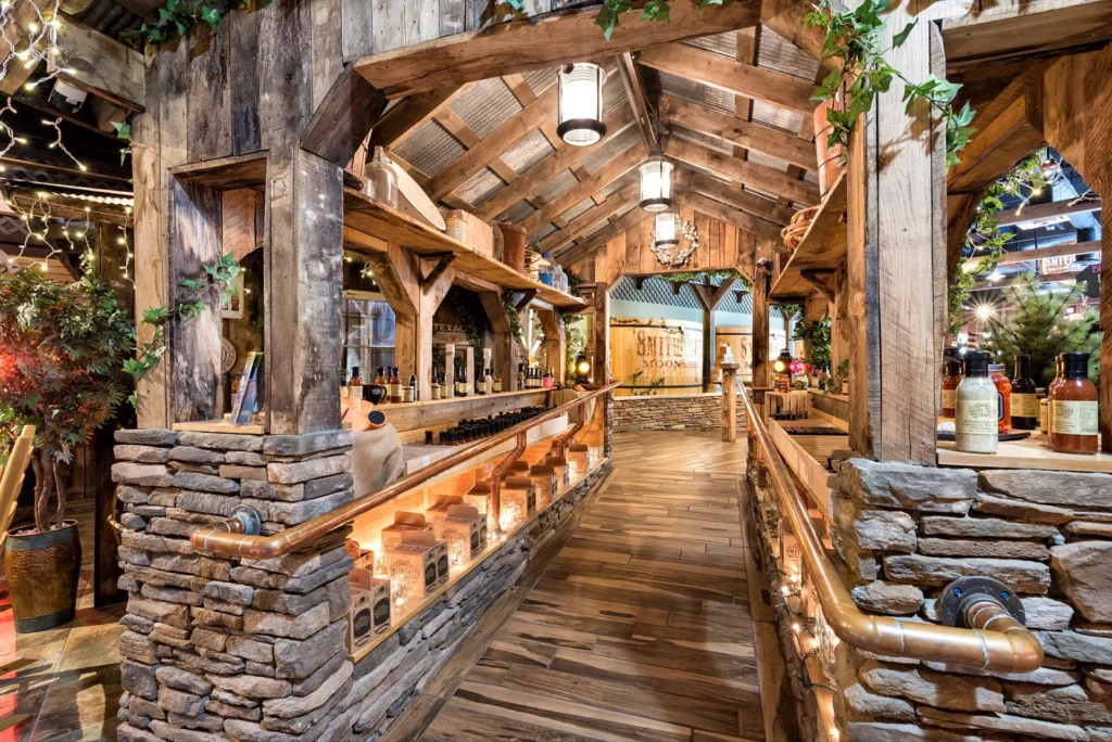Rustic interior of Smith Creek Moonshine retail space featuring wooden beams, stone accents, and illuminated shelves displaying bottles, designed and built by George Ewart, a top commercial architect firm in Knoxville, TN.