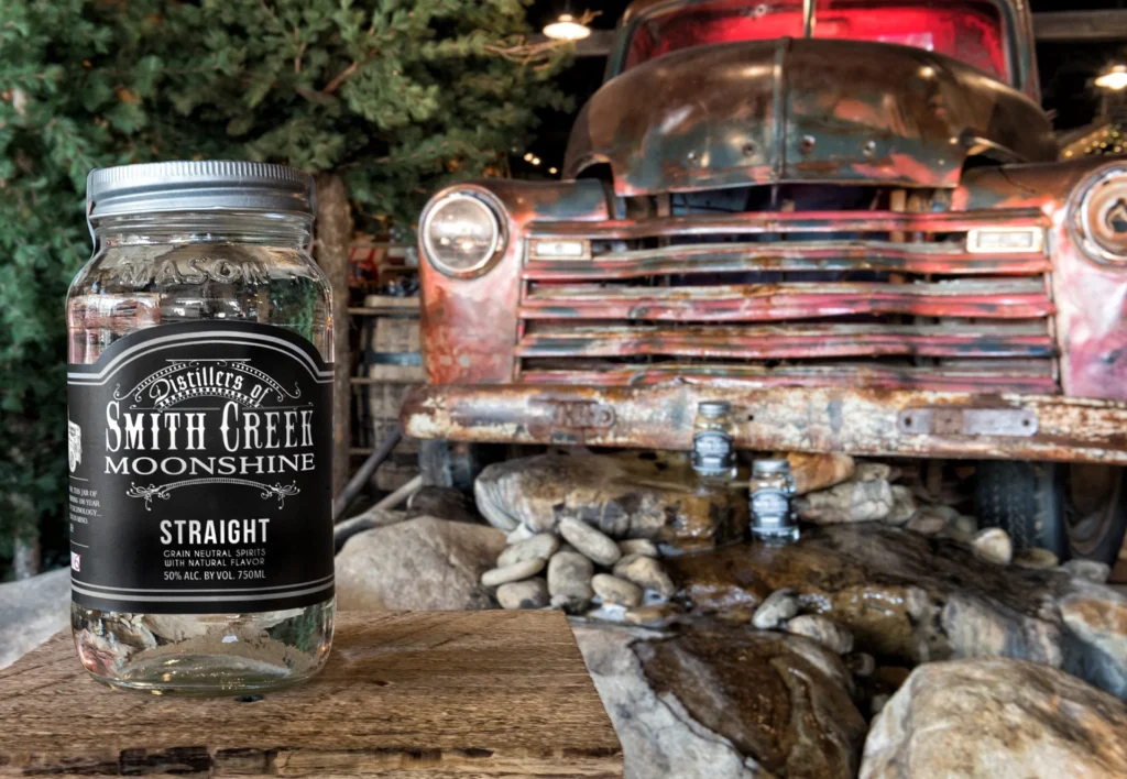 Jar of Smith Creek Moonshine in front of a vintage pickup truck, showcasing rustic design elements and an outdoor-inspired retail space, designed and built by George Ewart, a top commercial architect firm in Knoxville, TN.