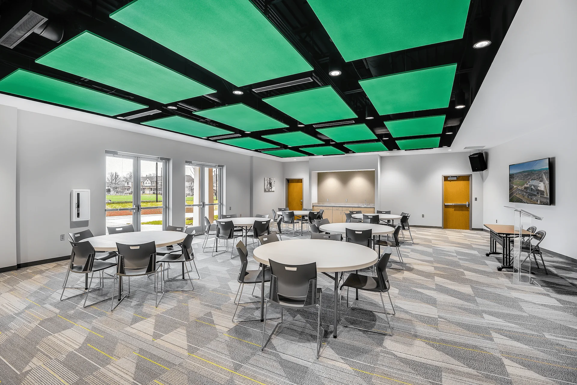 Community room in the Emerald Haslam Sansom Ministry Complex featuring circular tables, modern chairs, a vibrant green ceiling design, and large windows, designed and built by George Ewart, a top commercial architect firm in Knoxville, TN.