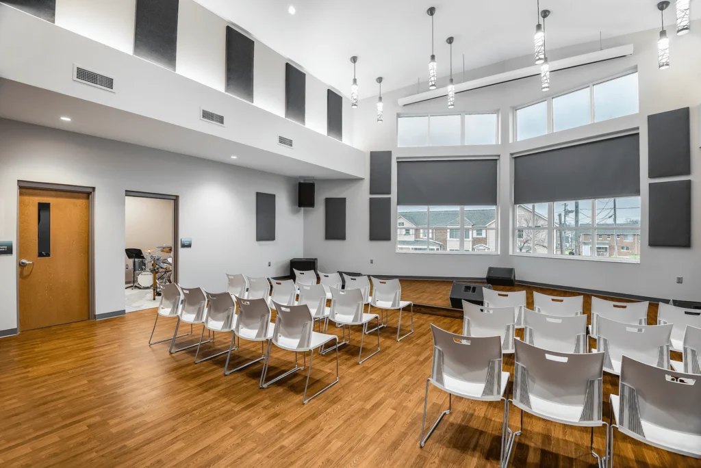 Interior view of the Emerald Youth community center's performing arts room, featuring rows of white chairs, large windows, and a wooden floor, designed and built by George Ewart, a top commercial architect firm in Knoxville, TN.