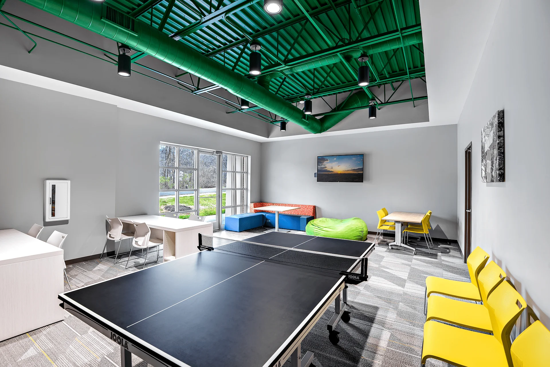 Interior view of the Emerald Haslam Sansom Ministry Complex featuring a ping pong table, colorful seating areas, and large windows, designed to foster youth development and community engagement in Knoxville, TN, by George Ewart, a top commercial architect firm.