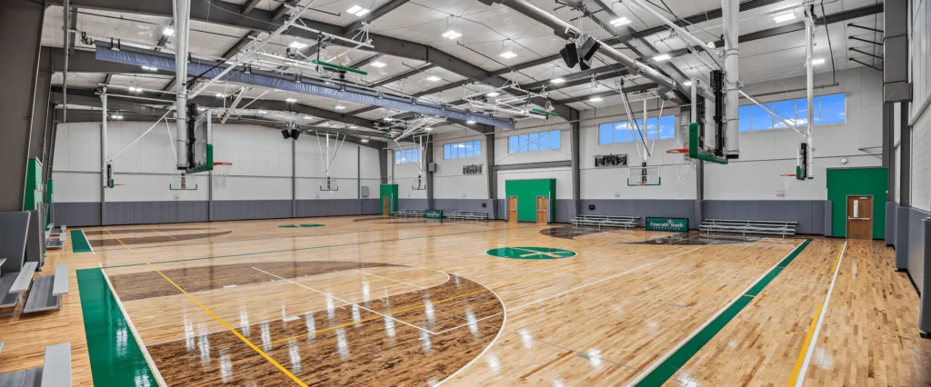 Indoor basketball court featuring polished wooden floors, multiple basketball hoops, and seating areas, designed for community engagement and youth development at the Emerald Youth Foundation center in Knoxville, TN, designed and built by George Ewart, a top commercial architect firm in Knoxville, TN.