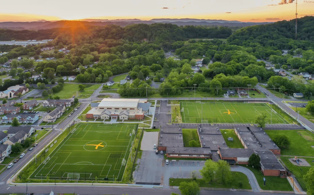 Aerial view of the Emerald Youth Foundation community center in Knoxville, TN, featuring two large outdoor multipurpose fields, a modern facility designed for youth development, and surrounding residential areas. Designed and built by George Ewart, a top commercial architect firm in Knoxville, TN.