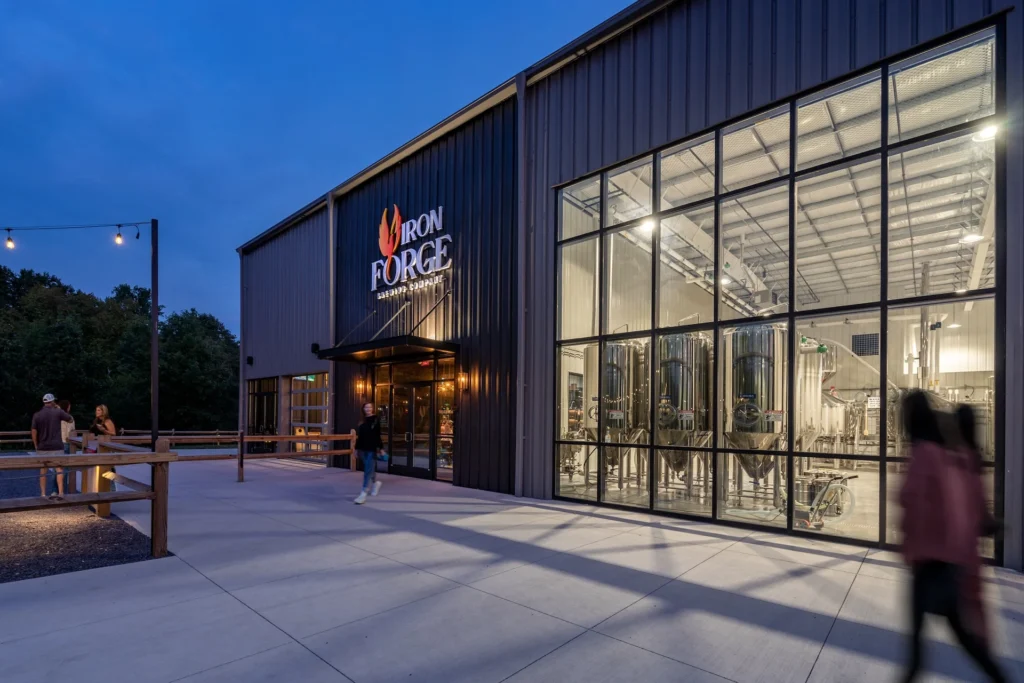 Iron Forge Brewing Co. exterior at dusk showcasing large glass windows revealing beer fermenters, designed and built by George Ewart, a top commercial architect firm in Knoxville, TN.