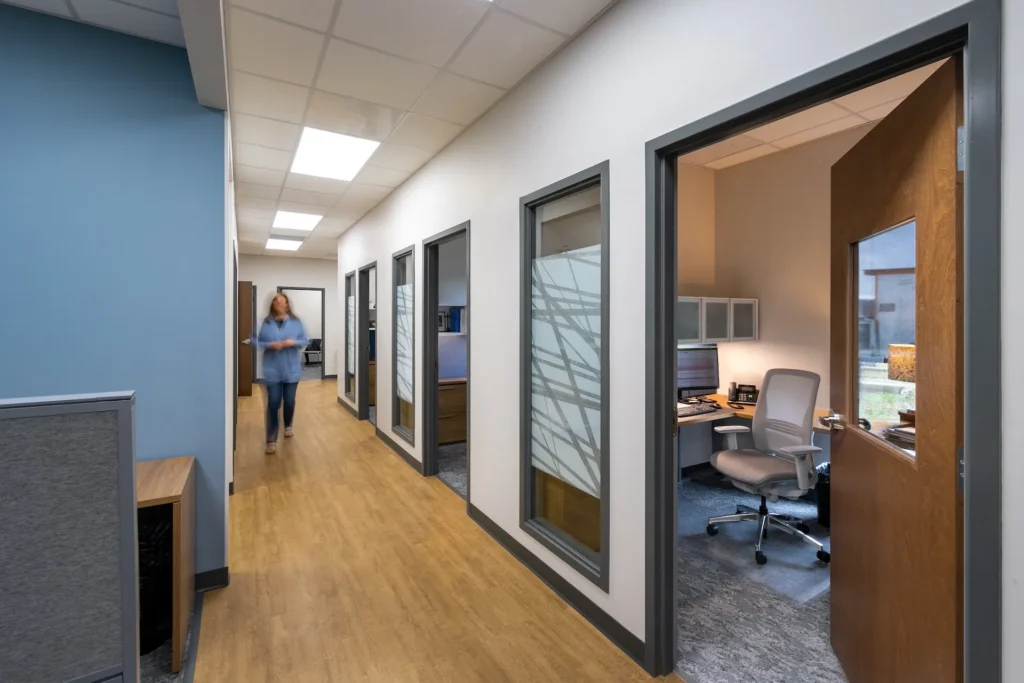 Hallway of renovated Catholic Charities facility in Knoxville, TN, featuring office doors, modern finishes, and a person walking, designed and built by George Ewart, a top commercial architect firm in Knoxville, TN.