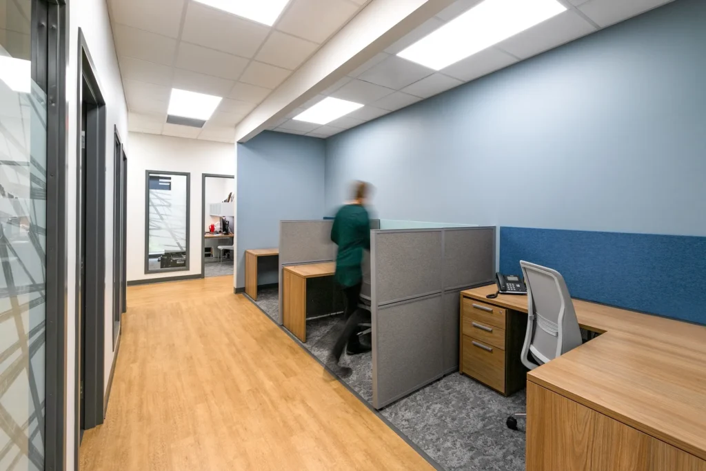 Modern office interior featuring shared workspace with cubicles, wooden desks, and a calming blue color scheme, designed and built by George Ewart, a top commercial architect firm in Knoxville, TN, enhancing workflow for Catholic Charities of East Tennessee.