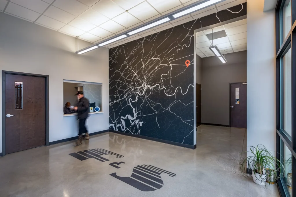 Interior view of Fraley & Schilling headquarters in Knoxville, TN, featuring a custom wall map, logo on polished concrete floor, and a reception area with a person interacting at the counter, designed and built by George Ewart, a top commercial architect firm in Knoxville, TN.