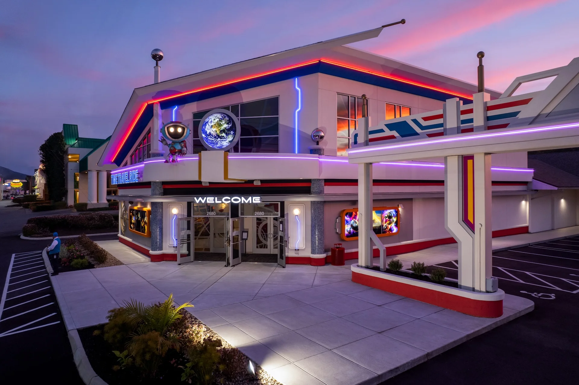 Exterior view of the Truth Traveler attraction featuring vibrant neon lights, a welcoming entrance with "WELCOME" signage, and a planet display, designed and built by George Ewart, a top commercial architect firm in Knoxville, TN.