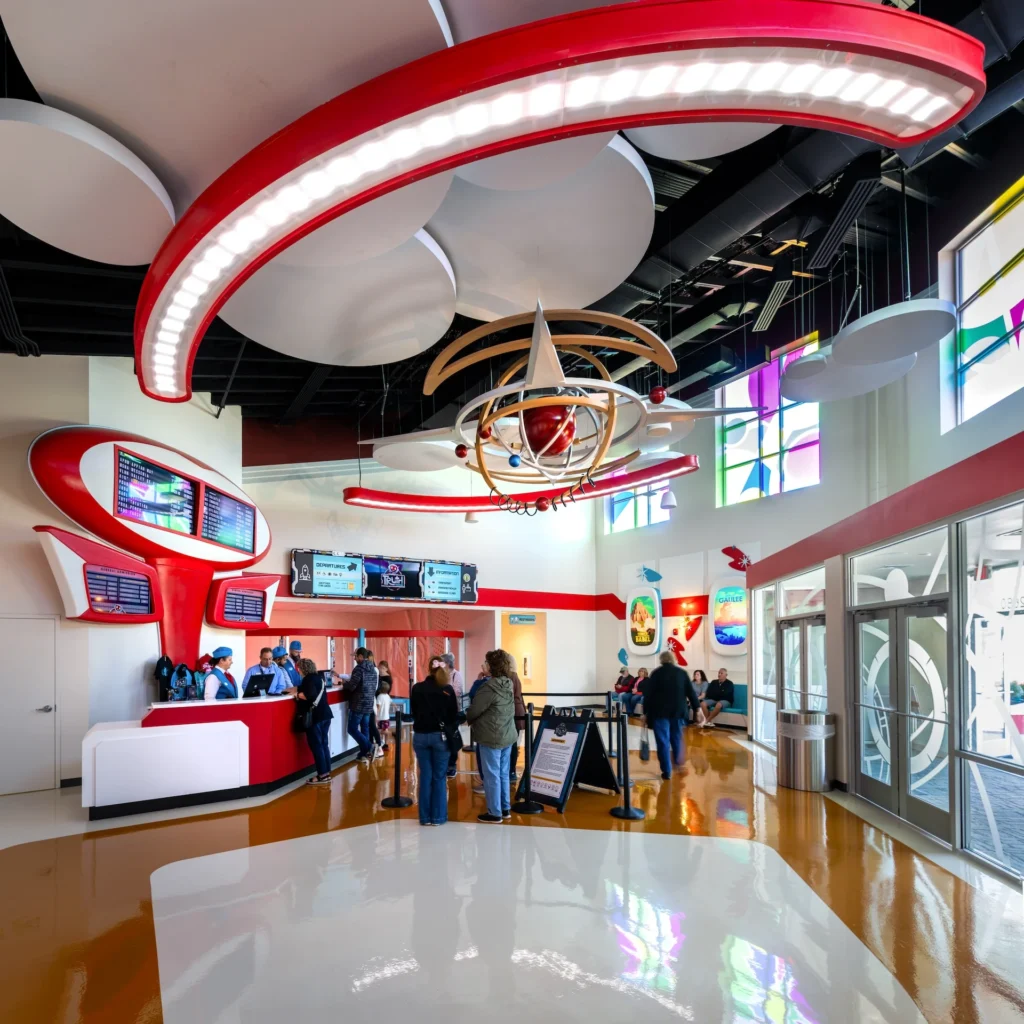 Futuristic lobby design of the Truth Traveler attraction in Pigeon Forge, featuring vibrant red accents, a striking overhead light fixture, digital display screens, and guests queuing at the reception area, designed and built by George Ewart, a top commercial architect firm in Knoxville, TN.