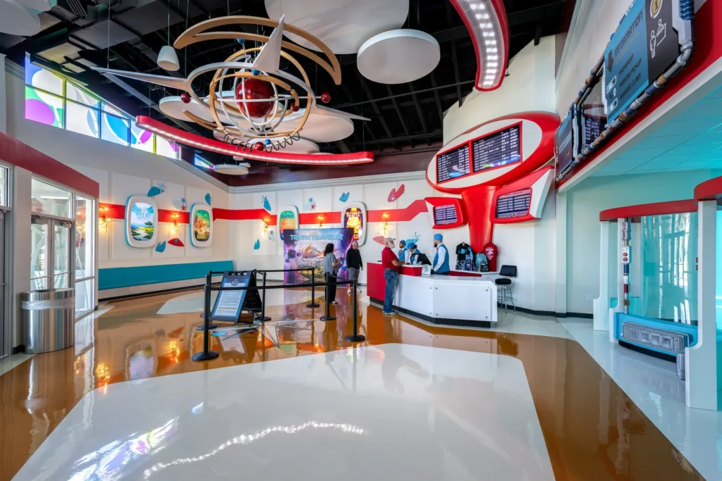 Futuristic lobby of the Truth Traveler attraction in Pigeon Forge, featuring vibrant decor, a central hanging sculpture, ticketing area, and promotional signage, designed and built by George Ewart, a top commercial architect firm in Knoxville, TN.