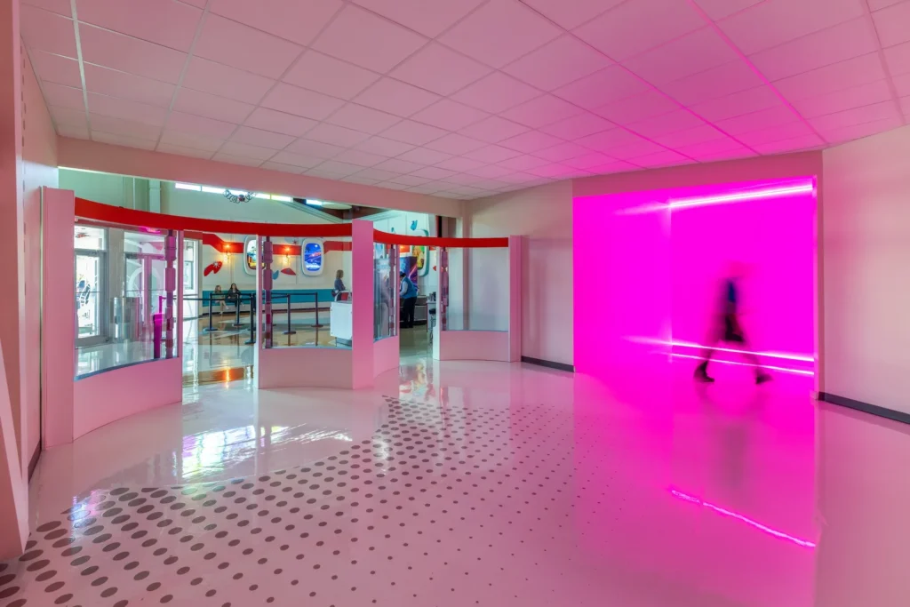 Futuristic lobby design with pink lighting, curved glass partitions, and a polished floor, part of the immersive Truth Traveler attraction in Pigeon Forge, designed and built by George Ewart, a top commercial architect firm in Knoxville, TN.