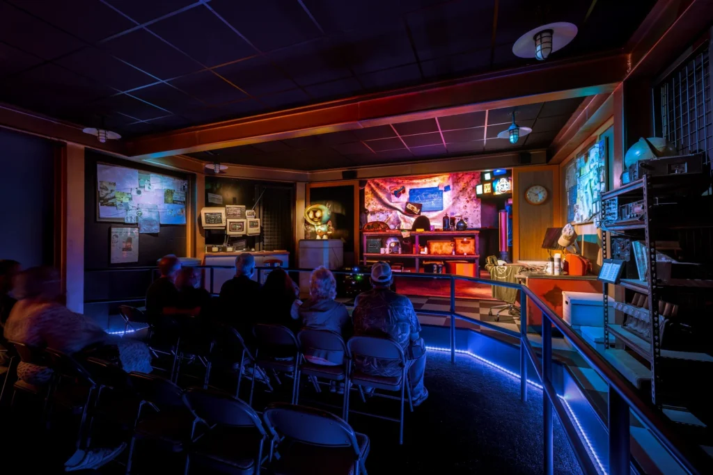 Interior view of the Truth Traveler attraction in Pigeon Forge, featuring immersive lighting, audience seating, and a themed backdrop with monitors and artifacts, designed and built by George Ewart, a top commercial architect firm in Knoxville, TN.