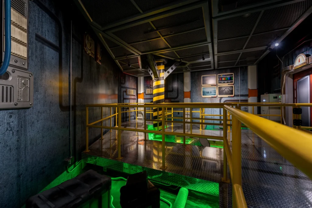 Futuristic interior of the Truth Traveler attraction in Pigeon Forge, featuring metallic structures, vibrant green lighting, and industrial design elements, designed and built by George Ewart, a top commercial architect firm in Knoxville, TN.