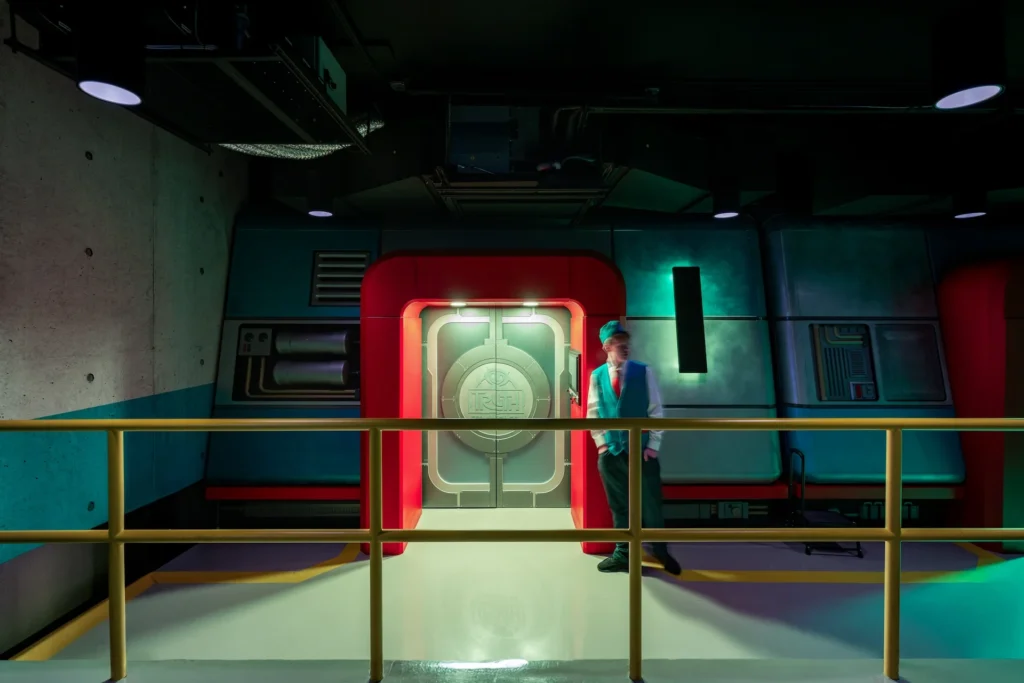 Futuristic lobby design of the Truth Traveler attraction in Pigeon Forge, featuring a vibrant red and teal color scheme, a prominent door with circular emblem, and a staff member in a vest, designed and built by George Ewart, a top commercial architect firm in Knoxville, TN.