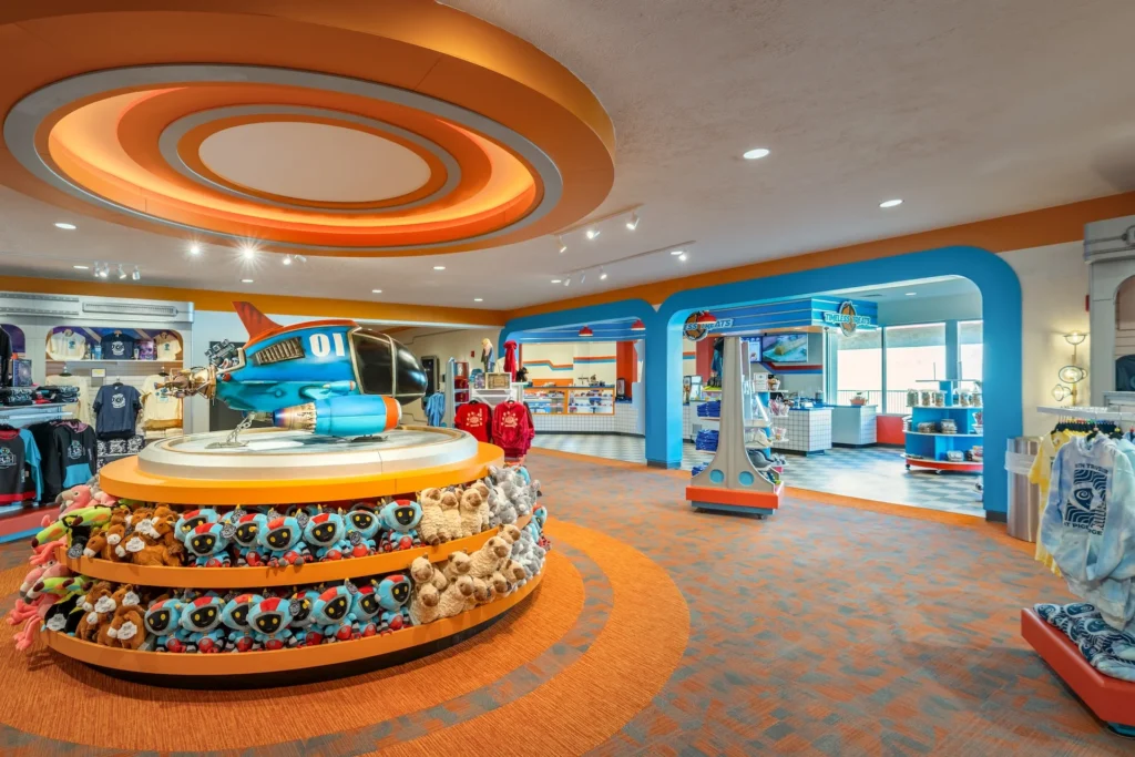 Colorful retail space featuring a blue and orange airplane display atop a circular pedestal, surrounded by plush toys and merchandise, designed for an immersive shopping experience in Pigeon Forge, Tennessee, emphasizing the attraction's family-friendly theme. Designed and built by George Ewart, a top commercial architect firm in Knoxville, TN.